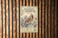 A vintage-style metal sign with a bird illustration and text, mounted on a wooden wall.