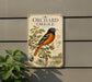 a vintage-style metal sign with an illustration of an oriole bird perched on a branch with berries, set against a backdrop of a tree and a house.