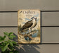 a vintage-style metal sign with an illustration of an osprey, a bird of prey, perched on a branch with a fish in its talons. The sign is mounted on a wall and is surrounded by greenery, including a plant to the left.