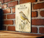 a vintage-style metal sign with a detailed illustration of a yellow warbler bird perched on a branch, mounted on a brick wall.