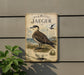 a vintage-style metal sign with a bird illustration, mounted on a wall next to a plant.