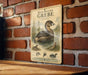 A vintage-style illustration of a pied billed grebe, a type of water bird, is displayed on a brick wall.