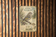 a vintage-style metal sign with illustrations of pine trees and birds, mounted on a wooden wall.