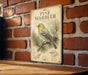 a vintage-style metal sign with a detailed illustration of a yellow bird perched on a pine branch, set against a brick wall background.