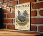 A vintage-style metal sign featuring a black and white illustration of a Plymouth Rock chicken, mounted on a brick wall.