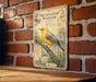 a vintage-style metal sign with a yellow bird perched on a branch, mounted on a brick wall.
