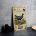 A vintage-style metal sign featuring illustrations and text about the purple Gallinule, a type of water bird, is displayed on a table.