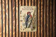 a vintage-style metal plaque with an illustration of a red-breasted sapsucker, a type of woodpecker, perched on a tree trunk.