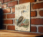 a vintage-style illustration of a red-footed booby, a type of seabird, perched on a branch against a brick wall.