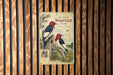 A vintage-style metal sign featuring illustrations of two red-headed woodpeckers perched on a tree stump, with a background of pine trees and a river.