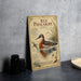 A vintage-style metal sign with illustrations and text about the Red Phalarope, a type of water bird, is displayed on a gray countertop.