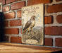 A vintage-style metal sign featuring an illustration of a red-tailed hawk with the text "RED-TAILED HAWK WITH PREY" and "WILDCATS" printed on it, mounted on a brick wall.