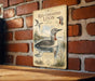 A vintage-style metal sign with illustrations of birds, including a large bird with a red throat, is mounted on a brick wall.