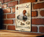 The image is a vintage-style illustration of a redhead duck, featuring detailed illustrations of the duck's head, body, and surrounding environment.