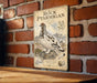 A vintage-style metal sign with a detailed illustration of a bird, likely a pterodactyl, perched on a rock against a brick wall.