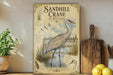 a vintage-style poster of a sandhill crane in a wetland, with illustrations of the crane and its natural habitat. The poster is displayed on a shelf next to a wooden cutting board and a potted plant.