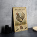 a metal sign with an illustration of a chicken, placed on a table next to some black camera lenses.