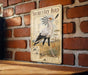 a decorative metal plaque with an illustration of a bird, mounted on a brick wall.