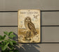 a metal sign with an illustration of a short-eared owl, mounted on a wall next to a plant.