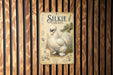 A metal sign with an illustration of a white chicken, labeled "Silkie Chicken", is displayed against a wooden background.