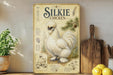 a vintage-style illustration of a Silkie chicken, which is a breed of chicken known for its fluffy white feathers and distinctive appearance. The illustration is displayed on a wooden shelf, accompanied by a potted plant, a cutting board, and some lemons.