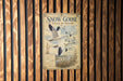 A vintage-style sign with the text "Snow Goose Flock in Flight" is displayed on a wooden wall.