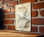 A vintage-style metal sign featuring an illustration of a snowy owl in flight, mounted on a brick wall.