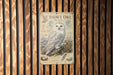 A metal sign featuring an illustration of a snowy owl, with text describing the bird species.