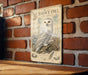 A vintage-style metal sign featuring an illustration of a snowy owl perched on a branch, with additional text and illustrations related to the species.