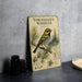 a metal sign with a bird illustration, placed on a table next to some black camera lenses.