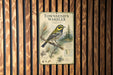 A metal sign with a bird illustration and text, mounted on a wooden wall.