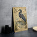 a metal sign with a detailed illustration of a tricolored heron, surrounded by various elements such as a bird, a birdhouse, and a bird feeder.