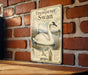 A metal sign with an illustration of a white swan on a brick wall, featuring text and a bird illustration.