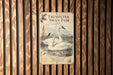 a sign for the "Trumpeter Swan Pair" located in the woods, with a wood fence in the background.