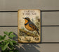 a vintage-style metal sign with a detailed illustration of a bird, likely a thrush, perched on a branch with pine cones. The sign is mounted on a wall and is surrounded by greenery, including a plant.