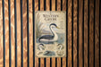 a vintage-style metal sign with illustrations of birds, including a large bird with a long neck and a smaller bird, set against a wooden background.