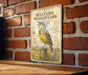 A vintage-style metal sign featuring a yellow bird, likely a meadowlark, perched on a wooden post against a brick wall.