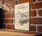 A metal sign with a bird illustration and text is mounted on a brick wall.