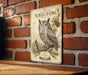 A metal sign featuring an illustration of a Western Screech- Owl, mounted on a brick wall.