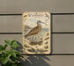 a metal sign with an illustration of a bird, likely a Whimbrel, standing on a beach. The sign also includes text and various bird-related illustrations.