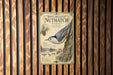 A vintage-style poster of a white-breasted nuthatch hanging on a wooden wall.