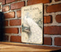 A vintage-style metal sign featuring an illustration of a white peacock against a brick wall background.