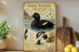 A vintage-style poster of a white-winged scoter, a type of water bird, is displayed on a wall next to a wooden cutting board and some potted plants.
