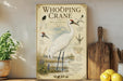 a poster of a Whooping Crane, a large white bird with a distinctive red head, standing in a grassy area with a body of water in the background. The poster includes illustrations and text that provide information about the Whooping Crane, such as its habitat, size, and behavior.