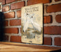 a vintage-style poster or sign with illustrations of two white cranes standing in a field, mounted on a brick wall.