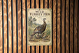 A vintage-style metal sign with an illustration of a turkey hen and its young, mounted on a wooden wall.