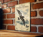 A vintage-style metal sign with a bird illustration and text, mounted on a brick wall.