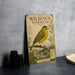 a vintage-style poster of a yellow warbler perched on a branch, with a detailed illustration of the bird and its natural surroundings.