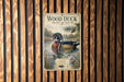 A vintage-style metal sign featuring a wood duck swimming in a pond, surrounded by pine trees and other natural elements.