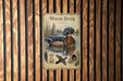 A vintage-style poster of a wood duck is displayed on a wooden wall, featuring a detailed illustration of the bird in its natural habitat.